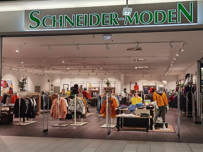 Innenansicht eines Modegeschäfts mit dem Schriftzug Schneider-Moden und ausgestellten Kleidung.