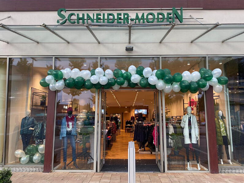 Außenansicht eines Modegeschäfts mit grünen und weißen Ballons und dem Schriftzug Schneider-Moden.