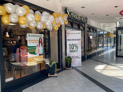 Schaufenster des Ladens Schneider-Moden mit goldenen und weißen Ballons und Rabattaktionen.