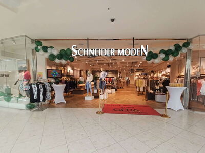 Innenansicht eines Modegeschäfts mit der Aufschrift Schneider Moden und grüner Dekoration.