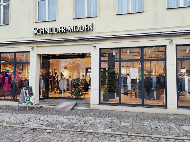 Außenansicht eines Modegeschäfts mit dem Schriftzug „Schneider-Moden“ und Schaufenstern.