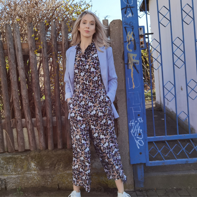 Frau in Jumpsuit und Blazer vor einem Zaun und blauer Tor.