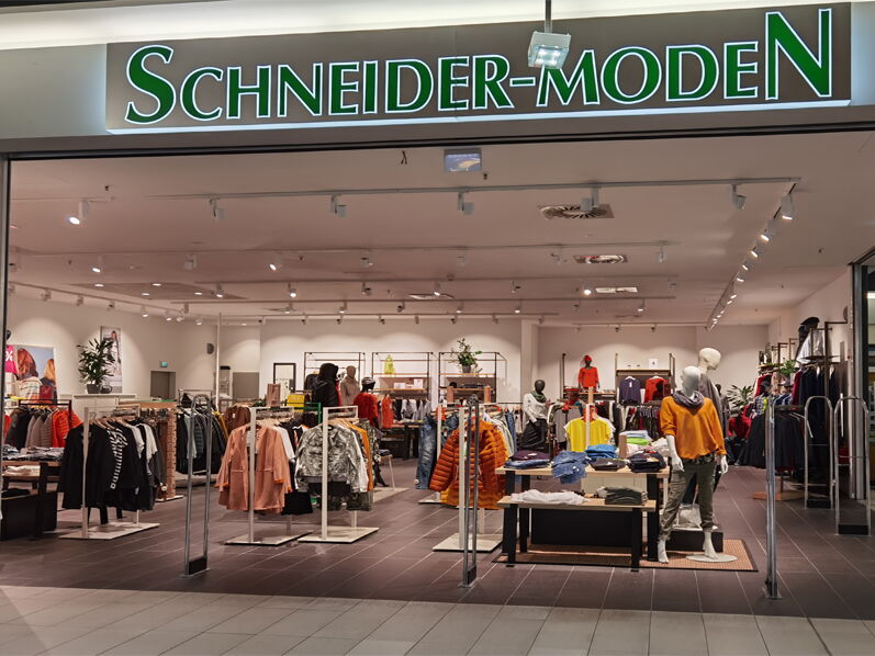 Innenansicht eines Modegeschäfts mit dem Schriftzug Schneider-Moden und ausgestellten Kleidung.